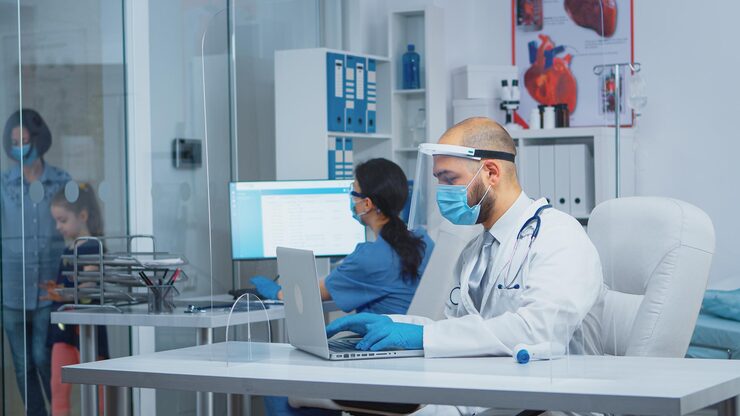 doctor with protection mask visor typing treatment laptop while mother comes with daughter consultation hospital coronavirus pandemic equipped nurse talking with patients 482257 14494